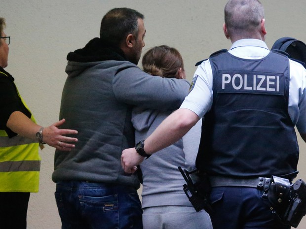 Um casal que aguardava o voo 4U9525 é escoltado por um policial e uma funcionária do aeroporto em Düsseldorf, na Alemanha (Foto: Frank Augstein/AP)