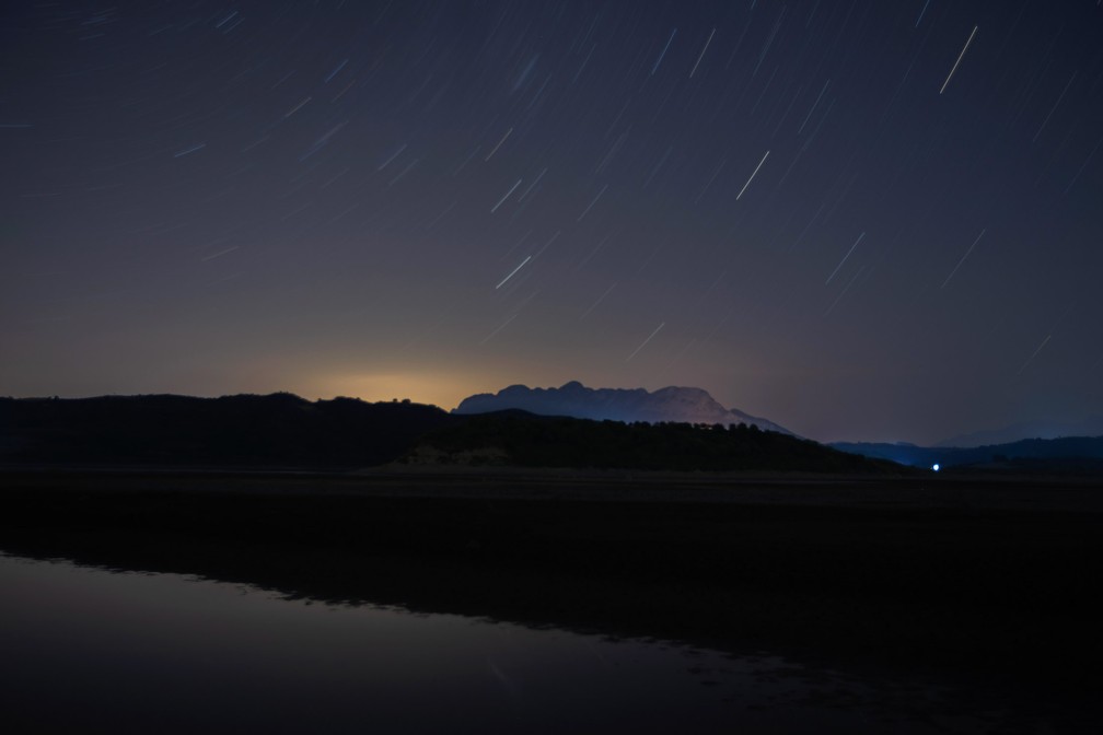 Nesta foto tirada com longo tempo de exposição, estrelas se movem no céu noturno durante a chuva de meteoros Perseidas no Lago Pineios, perto da vila de Velanidi, em Peloponeso, na Grécia, na quinta-feira (13) — Foto:  Petros Giannakouris/AP
