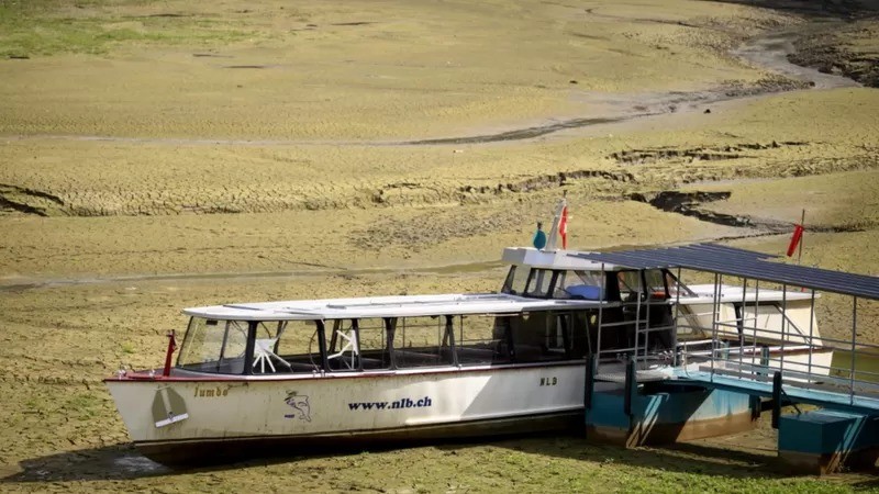 Seca está produzindo cenas como esta de um barco encalhado na lama da margem do Lago franco-suíço Brenets — agora seco (Foto: EPA via BBC)