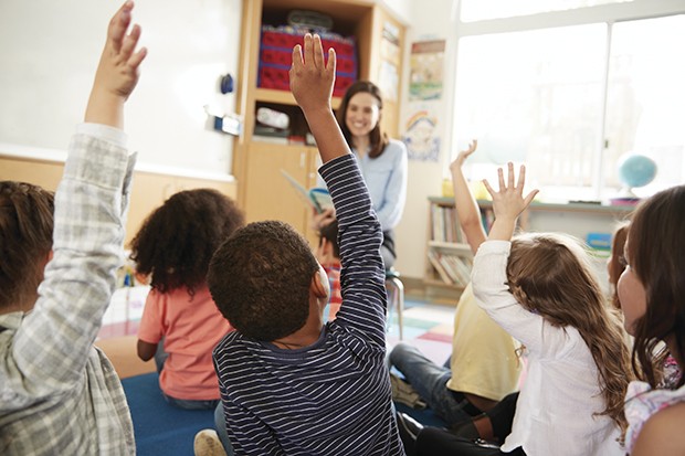 Elementary school kids raising hands to teacher, back view (Foto: Getty Images/iStockphoto)