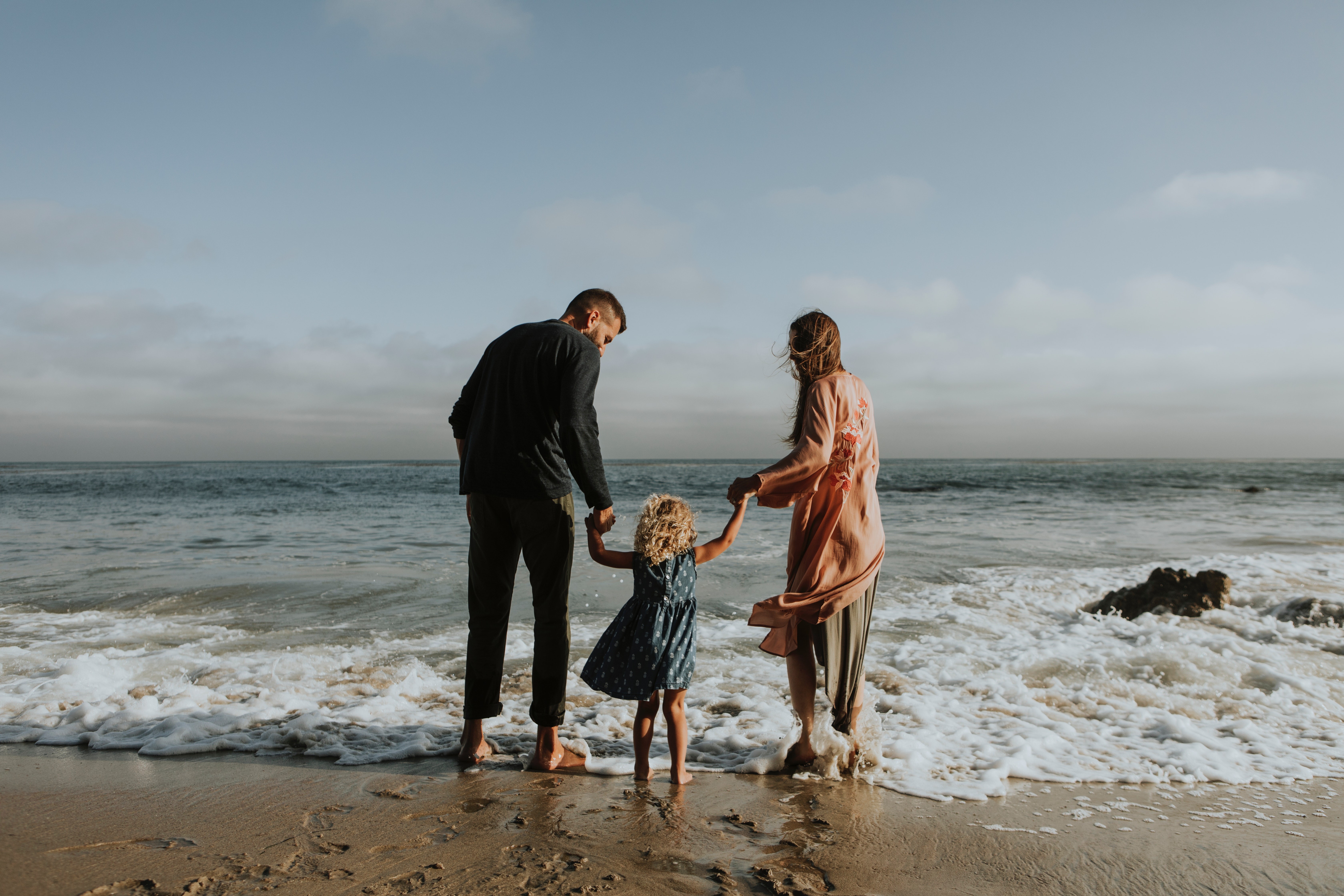 casal com criança na praia de mãos dadas (Foto: Pexels)