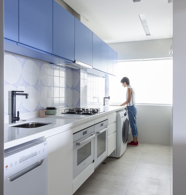 Cozinha e lavanderia estão integradas por uma grande bancada de Silestone que abriga todos os eletrodomésticos. No frontão, azulejos do ateliê Leopardi Esperante (Foto: Maíra Acayaba/Divulgação)