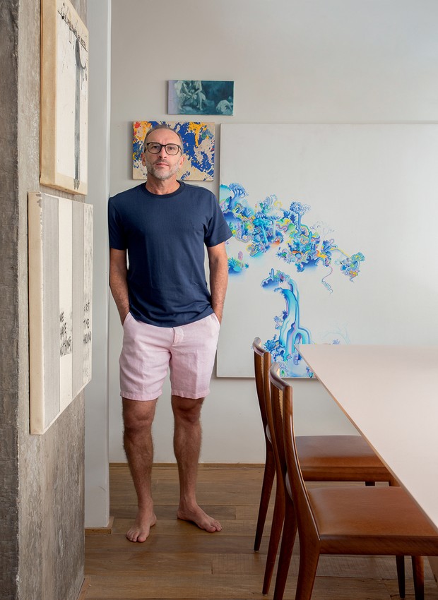 O morador, Denilson Machado, está na sala de jantar, com quadro branco e azul de Pedro Varela (Foto: Denilson Machado / MCA Estúdio / Divulgação)