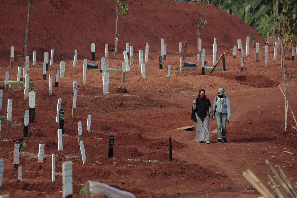 Muçulmanas indonésias andam em meio a túmulos em um cemitério em Jakarta, onde novas covas foram abertas para enterrar vítimas da Covid-19 no país, no dia 24 de setembro. — Foto: Dita Alangkara/AP