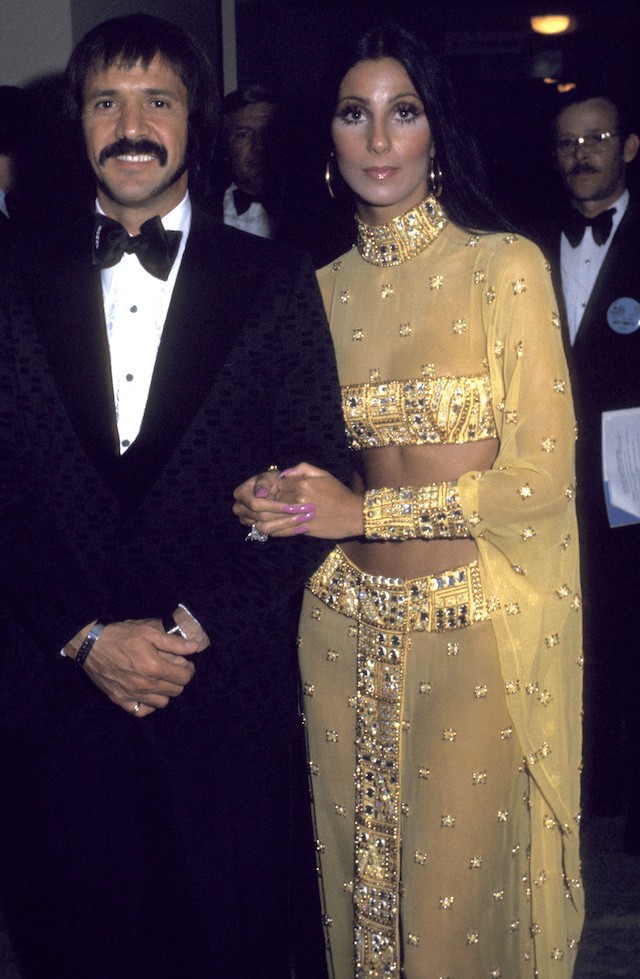 Cher no tapete vermelho do Oscar de 1973 ao lado de Sonny Bono usando um dos looks mais icônicos de sua carreira, que levou a barriguinha de fora para a noite de gala. (Foto: Getty Images)
