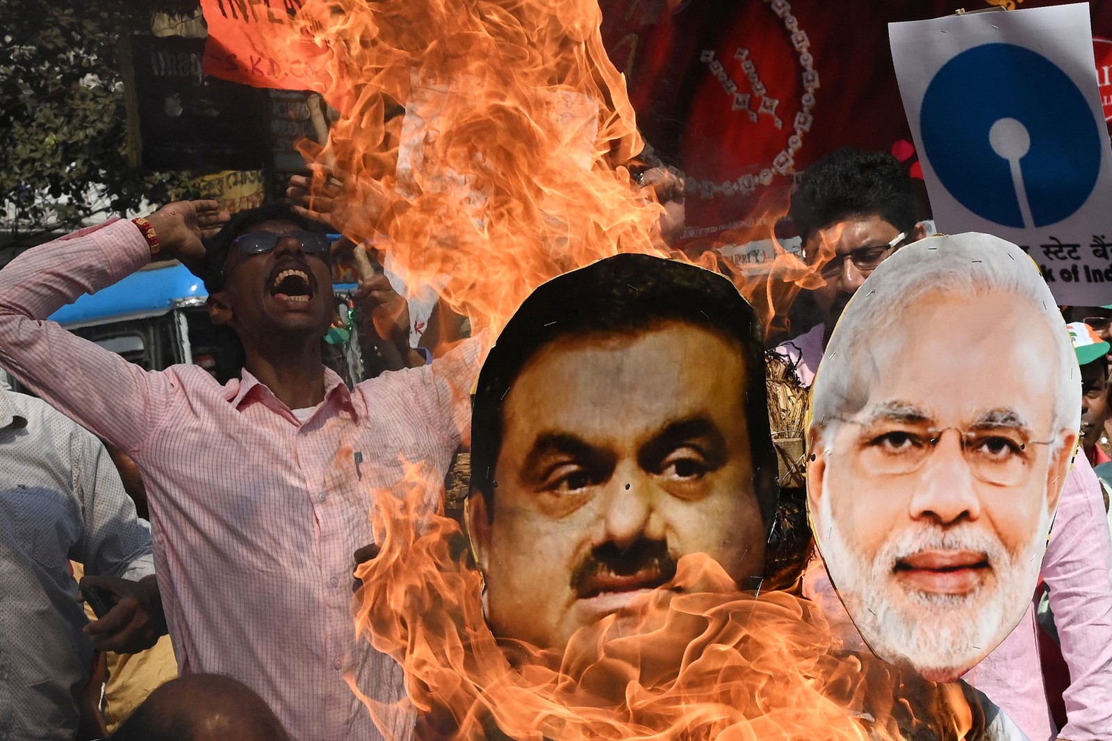 Ativista do Partido do Congresso da Índia queima as imagens do primeiro-ministro, Narendra Modi, e do magnata indiano Gautam Adani durante um protesto contra as políticas financeiras do governo sindical em Calcutá — Foto: Dibyangshu SARKAR / AFP