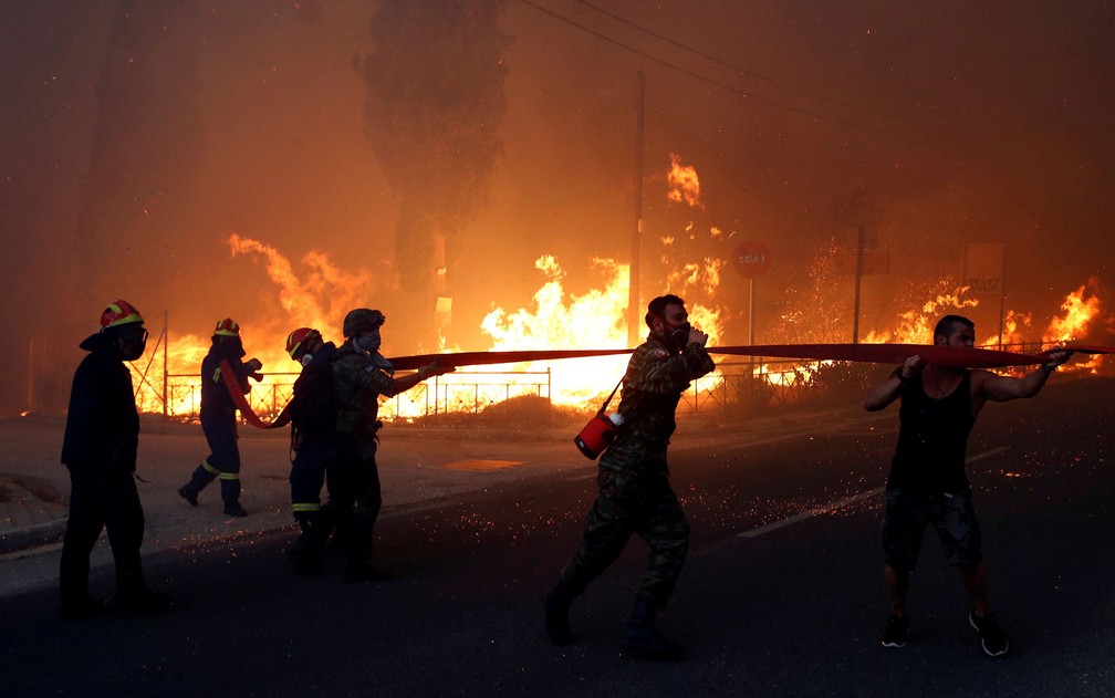 Bombeiros, soldados e moradores carregam mangueira para combater incêndio na cidade de Rafina, perto de Atenas, na Grécia, na segunda-feira (23) (Foto: Costas Baltas / Reuters)