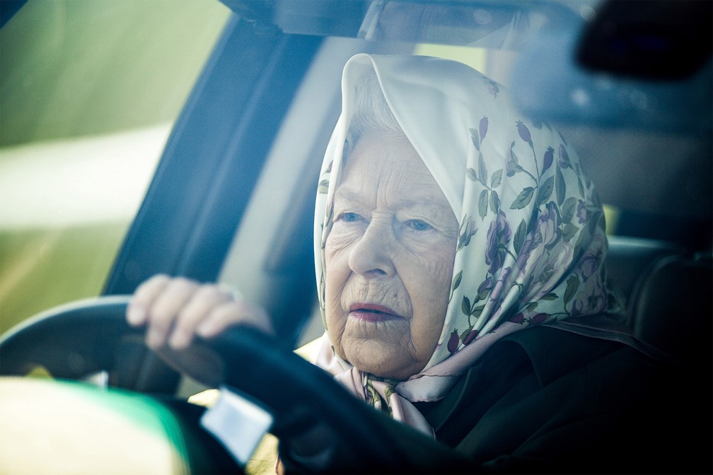 A rainha do Reino Unido, Elizabeth II, chega dirigindo seu carro à famosa corrida de cavalos anual Royal Windsor, em Windsor, a oeste de Londres. O evento é conhecido, entre outras coisas, por atrair visitantes com trajes exagerados — Foto: Daniel Leal-Olivas/AFP