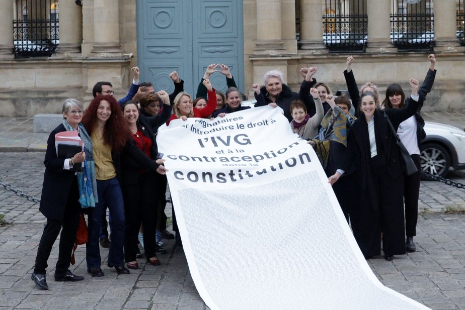 Membros do partido de esquerda francês França Insubmissa (LFI) e membros de associações pró-aborto comemoram com uma faixa depois que o Parlamento votou para incluir o direito ao aborto à Constituição, do lado de fora da Assembleia Nacional em Paris