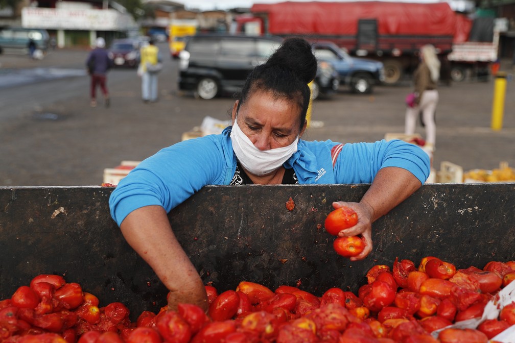 Com máscara, mulher procura por tomates ainda comestíveis entre os que foram descartados de mercado em Assunção, no Paraguai, na quarta-feira (6) — Foto: Jorge Saenz/AP Photo