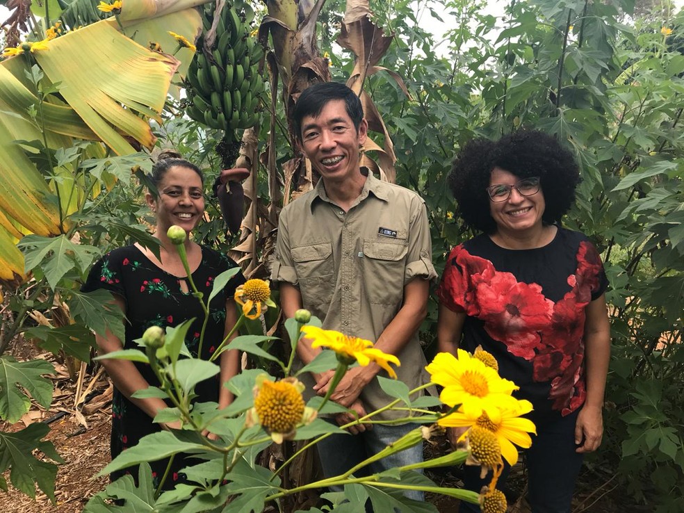 Dona da chácara, Gizelma Fernandes, o professor Leonardo e a vice-diretora da escola posam para foto em meio à agrofloresta — Foto: Marília Marques/G1