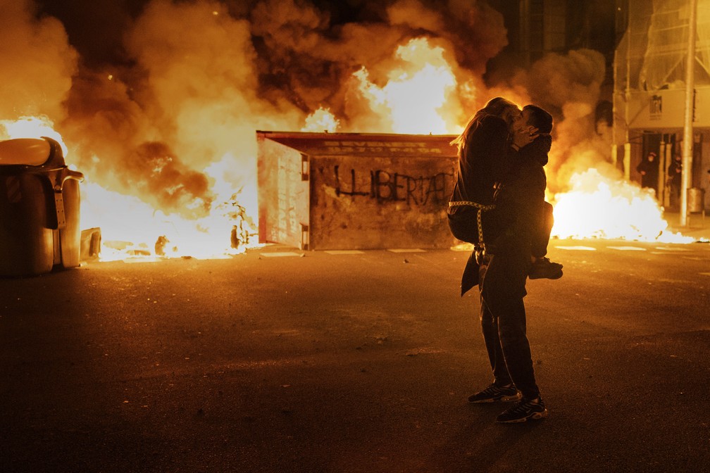 18 de fevereiro - Um casal se beijou em frente a uma barricada incendiada por manifestantes durante confrontos com a polícia após protesto condenando a prisão do cantor de rap Pablo Hasél, em Barcelona, ​​Espanha — Foto: Emilio Morenatti/AP