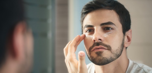 Young hispanic people and male beauty. Metrosexual man applying lotion for anti-aging treatment around eye (Foto: Getty Images/iStockphoto)