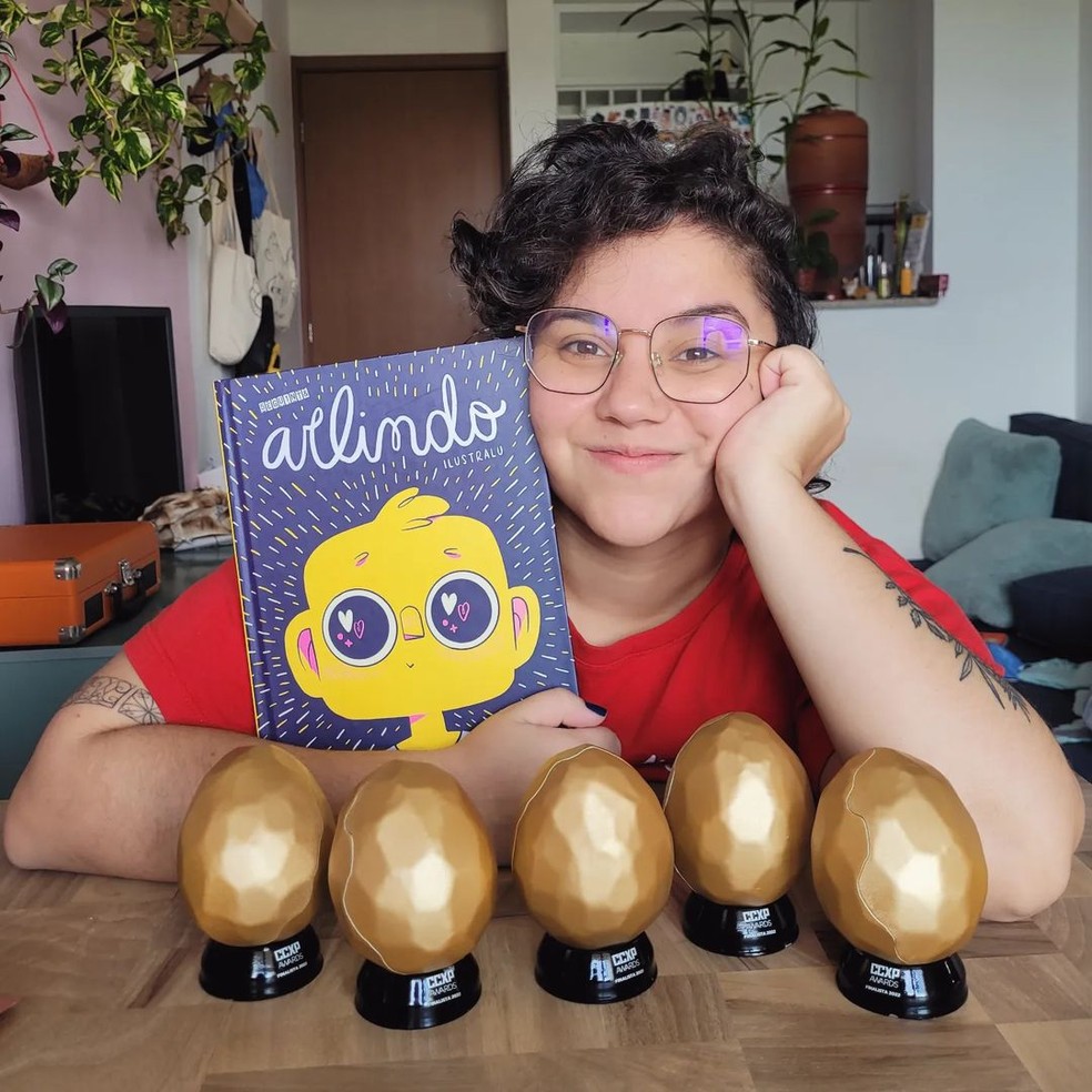Luiza Souza, a Ilustralu, com o livro Arlindo e "ovos" que representam as cinco indicações a prêmio na CCXP Awards — Foto: Redes sociais