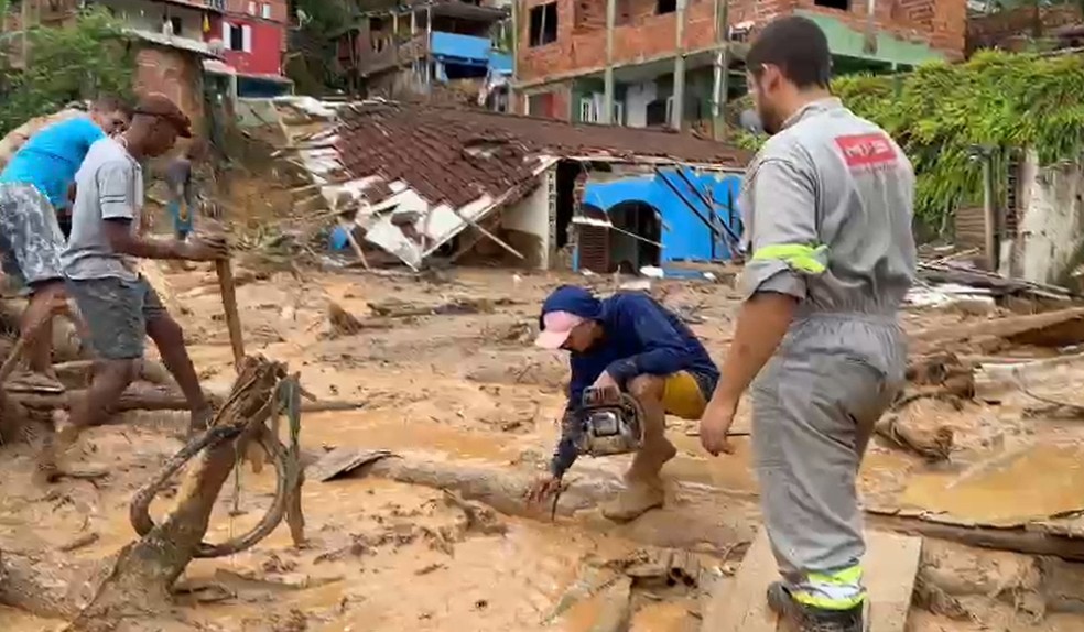Moradores tentam cortar troncos para terem acesso em São Sebastião — Foto: Bruno Tavares/TV Globo