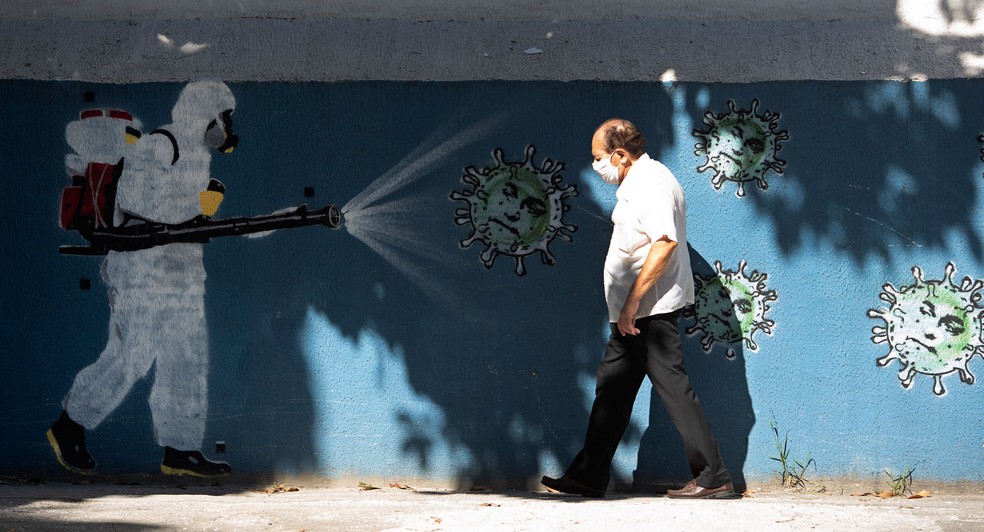 Homem passa por um mural representando um trabalhador com equipamento de proteção que desinfeta um novo coronavírus no Rio de Janeiro, na segunda-feira (22)  — Foto: Silvia Izquierdo/AP
