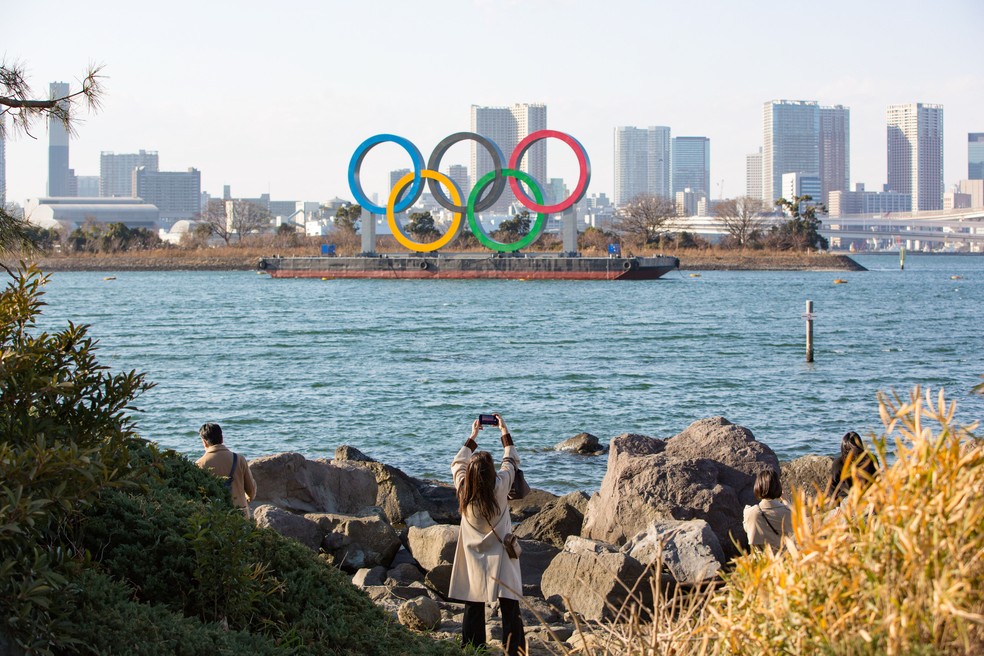 Visitante tira foto no Odaiba Marine Park com os anéis olímpicos na Marina de Tóquio ao fundo — Foto: Getty Images