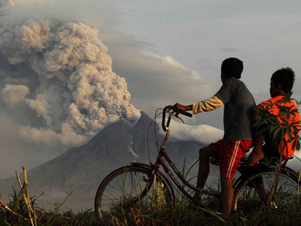 Crianças de bicicleta observam vulcão Merapi em atividade, na Indonésia (Foto: Andry Prasetyo/Reuters)