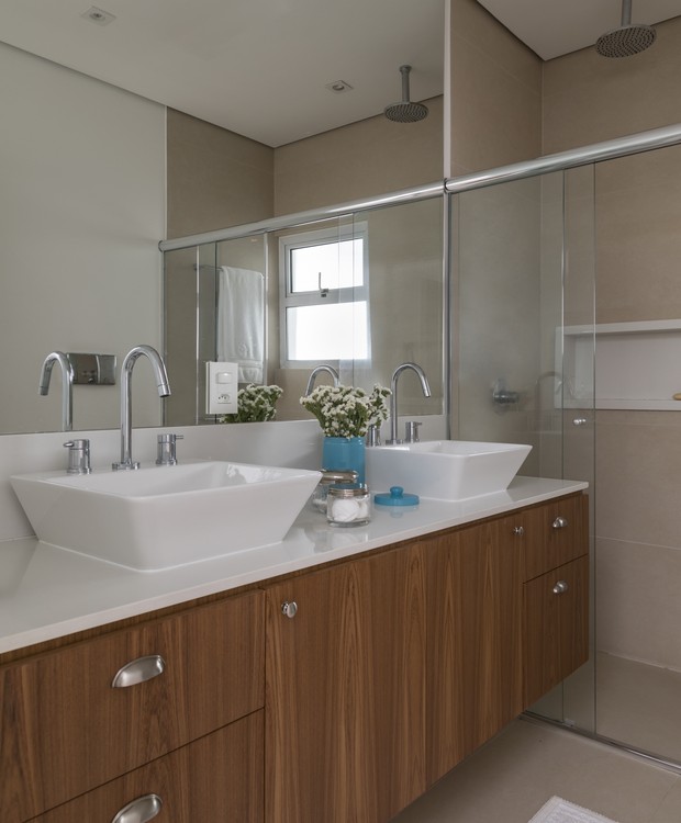O banheiro da suíte do casal mistura os acabamentos claros do piso e do porcelanato com a madeira dos gabinetes (Foto: Divulgação)
