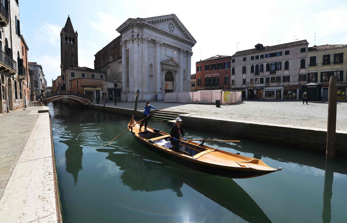 Duas mulheres, integrantes do grupo Row Venice, circulam pelos canais de Veneza, onde estão fazendo delivery em gôndolas para moradores que não podem sair de casaAFP