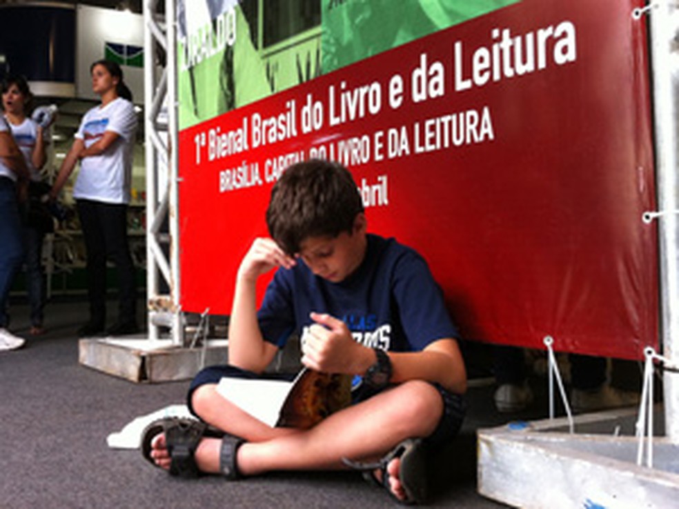 Gabriel Elias lê sentado no chão da bienal, em Brasília — Foto: Káthia Mello/G1
