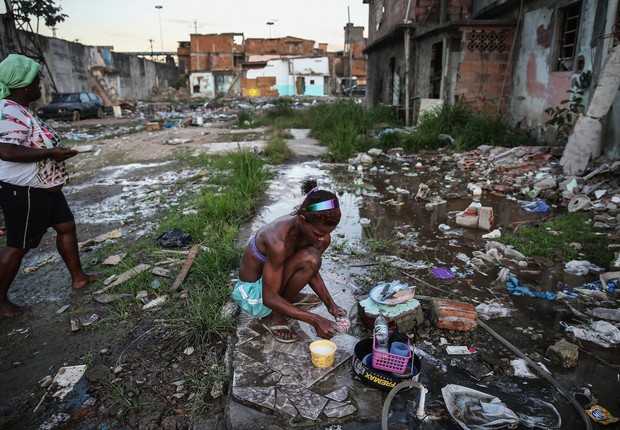 Jovem Alessandra lava utensílios de cozinha com mangueira em meio a ruínas de casas na comunidade Metro-Manguera, no Rio de Janeiro ; pobreza ; favela ;  (Foto: Mario Tama/Getty Images)