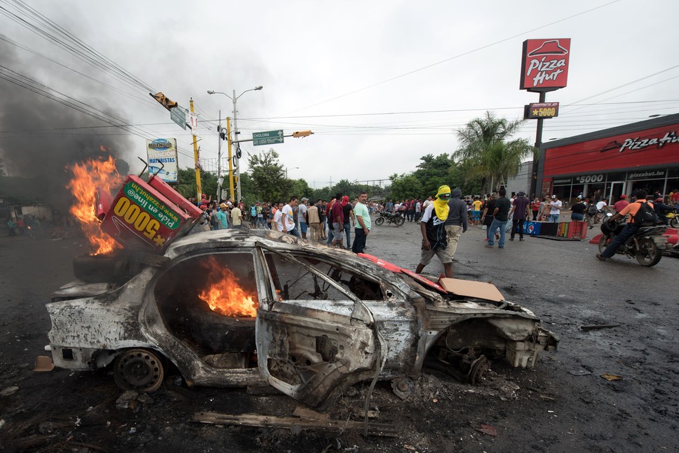 Carro é incendiado durante protesto por resultado das eleições presidenciais do último domingo em Honduras (Foto: Jordan Perdomo/AFP)