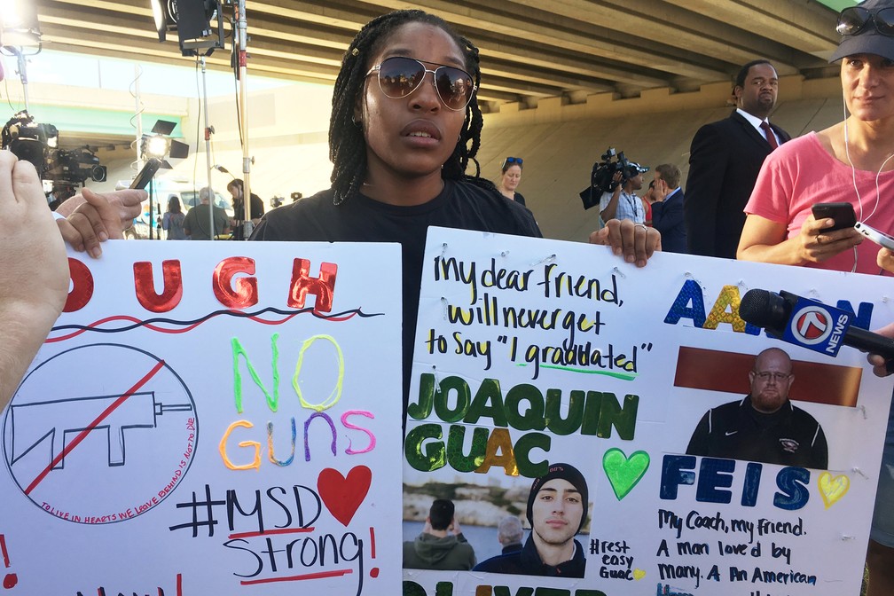 Tyra Hemans, aluna de 19 anos da Stoneman Douglas High School, exibe nesta quinta-feira (15) cartazes com homenagem a colega e professor perto do cordão policial montado na escola (Foto: Zachary Fagenson/Reuters)