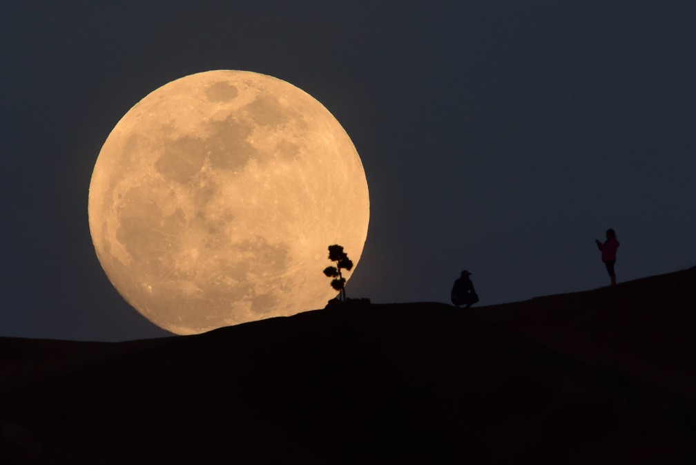 Uma pessoa posa para foto enquanto a lua nasce no parque Griffith, em Los Angeles, nos EUA, na noite de terça (30) (Foto: Robyn Beck/AFP)