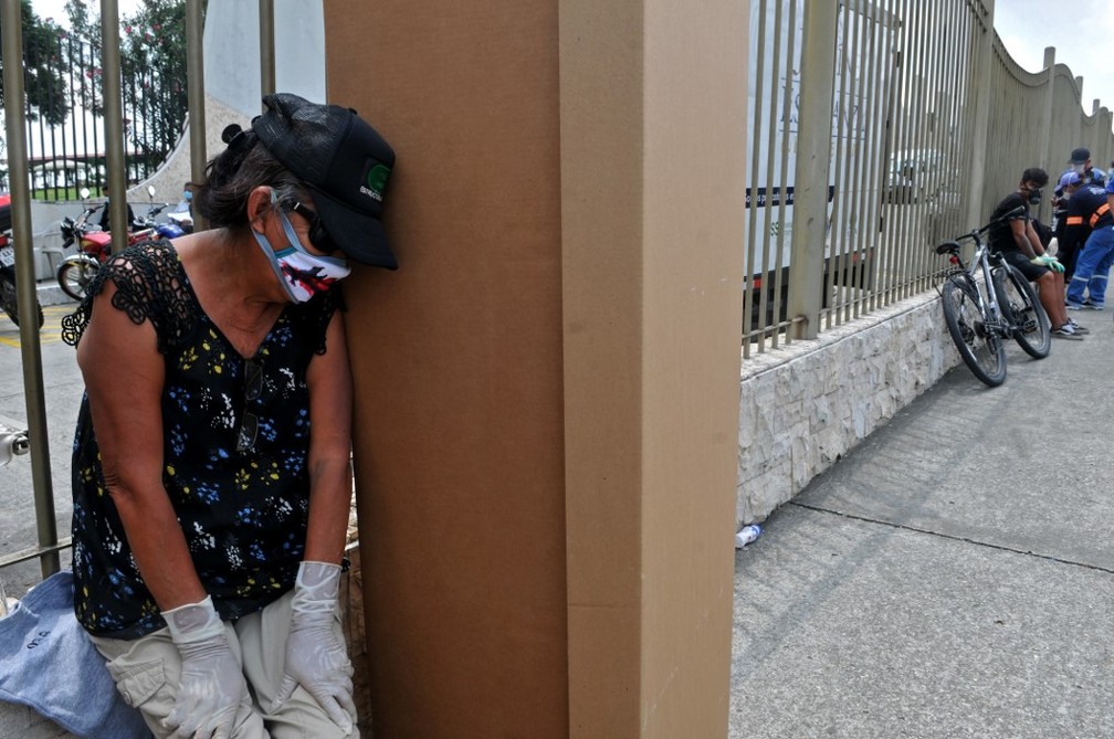 Mulher de máscara lamenta morte ao lado de caixão de papelão em cemitério de Guayaquil, no Equador — Foto: Jose Sanchez/AFP