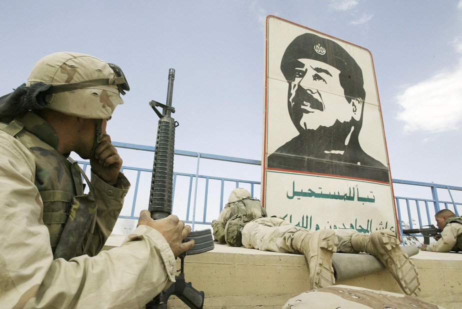 Fuzileiros navais dos EUA se posicionam perto de retrato do ditador iraquiano Saddam Hussein em um estádio em Bagdá