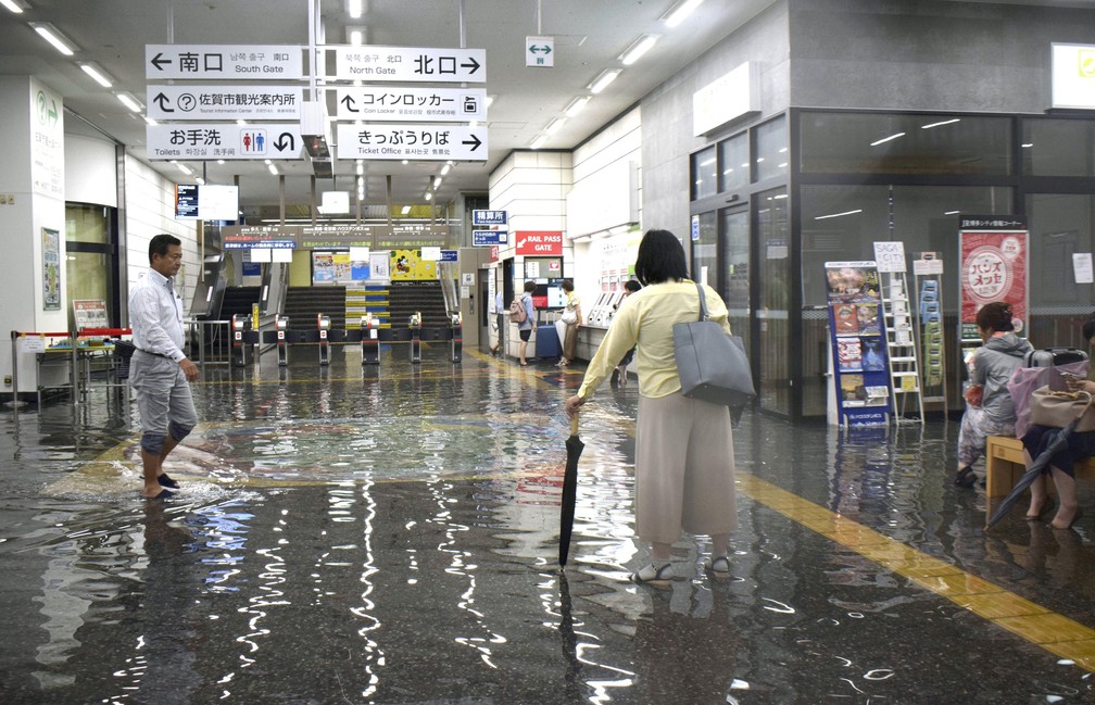 Pessoas andam por uma estação de trem inundada na região de Saga, no sul do Japão, nesta quarta-feira (28). — Foto: Kyodo News via AP
