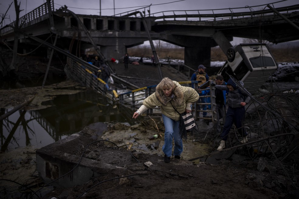 02/03 - Uma mulher corre enquanto foge com sua família por uma ponte destruída nos arredores de Kiev, na Ucrânia, nesta quarta-feira (02) — Foto: Emilio Morenatti/AP
