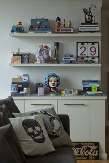 Prateleiras com livros e objetos decorativos, sofá preto com almofadas de caveira de Alexandre Herchcovitch. Projeto do designer e arquiteto Guto Requena
