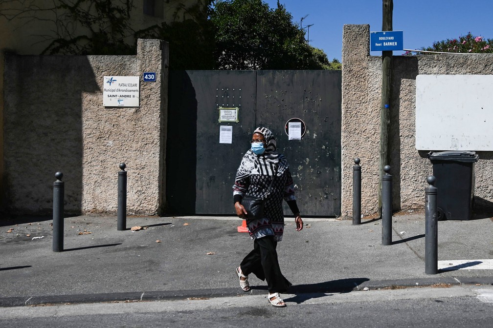 Mulher caminha nesta sexta-feira (4) em frente à entrada da escola primária Saint-André Condorcet fechada devido a um caso Covid-19, em Marselha, no sul da França  — Foto: Christophe Simon / AFP