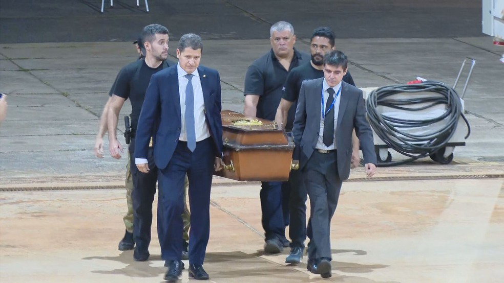 Delegado Sandro Avelar, diretor executivo da Polícia Federal (à esquerda) ajuda a carregar caixão com remanescentes humanos encontrados no Amazonas chega no Aeroporto de Brasília  — Foto: TV Globo/Reprodução