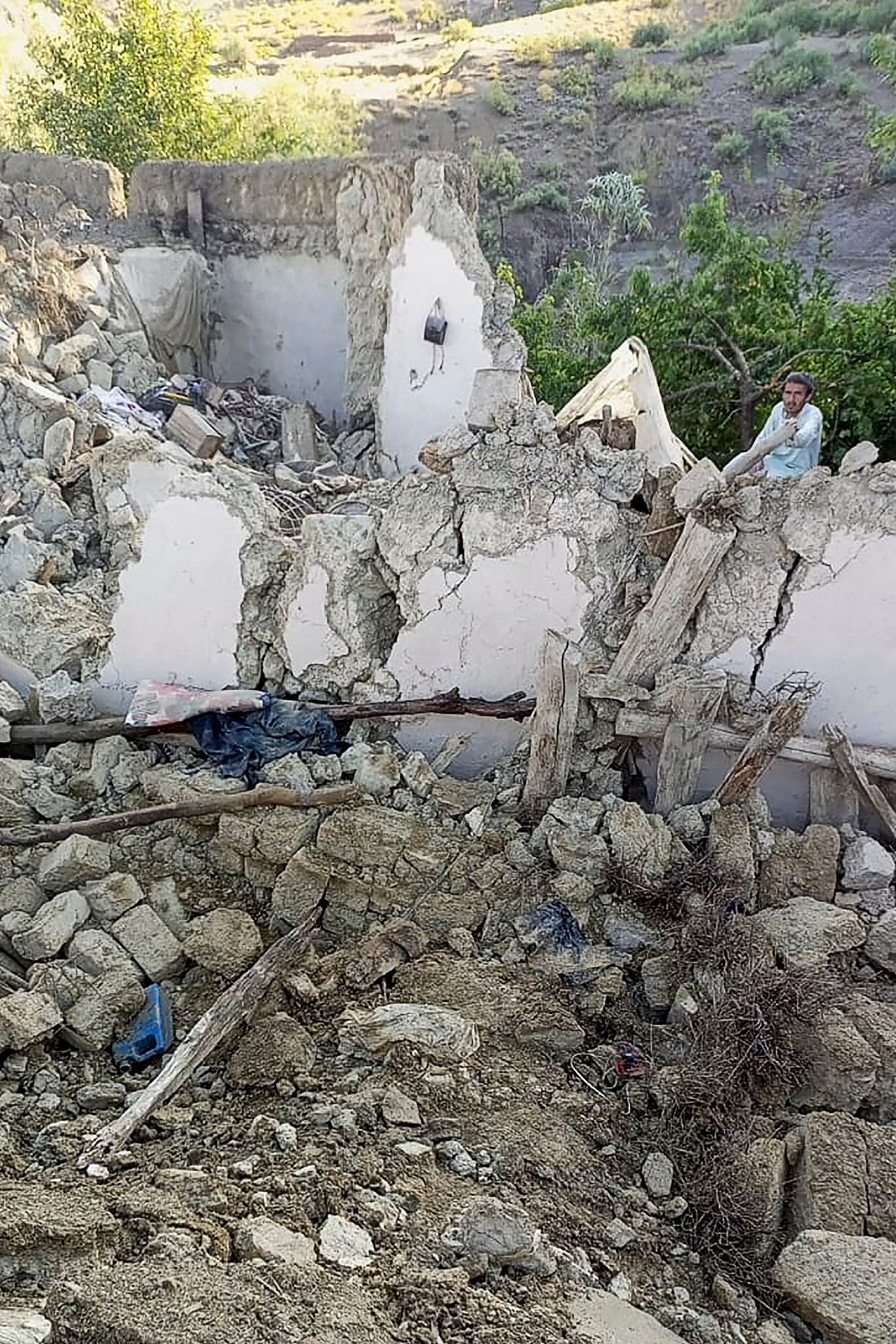 Homem é visto ao lado de uma casa que desabou após o terremoto no distrito de Gayan — Foto: Bakhtar News Agency / AFP