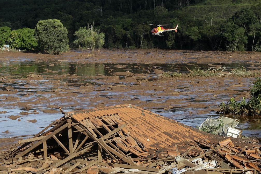 Equipes de resgate fazem busca de helicóptero em área inundada dois dias depois do rompimento da barragem da Vale, em Brumadinho. — Foto: André Penner/AP