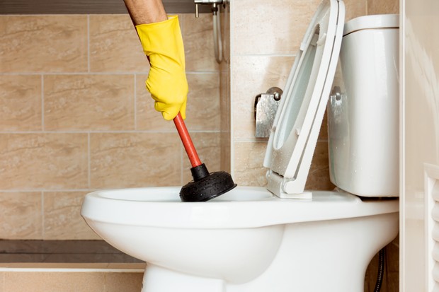 Human hand wearing yellow rubber gloves is using a device to fix a clogged toilet bowl. (Foto: Getty Images/500px)