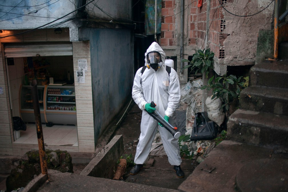 O líder comunitário Thiago Firmino, de 39 anos, posa para uma foto em traje de proteção ao desinfetar a favela de Santa Marta, no Rio de Janeiro, durante a pandemia de COVID-19. Thiago disse que está preparado para correr riscos e lutar por sua favela, onde nasceu e cresceu, onde vivem sua família e amigos. Segundo ele, a favela precisa combater seus próprios problemas, já que o governo não fará isso, e o coronavírus é apenas mais um problema para seus moradores, que morrem de balas perdidas e pela falta de acesso a todos os tipos de serviços públicos. Ele e seu irmão Tandy estão tentando proteger o bairro por amor, declarou — Foto: Mauro Pimentel/AFP