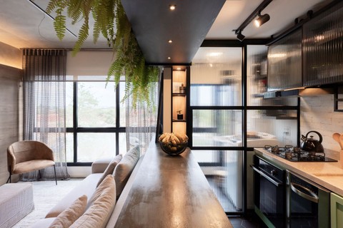 Neste apartamento de 60 m² reformado pelo escritório Braccini + Lima, sala e cozinha são integradas pela bancada. Ela marca a divisão entre os ambientes, permitindo que pessoas interajam em cômodos diferentes. O balcão ainda esconde as "costas" do sofá