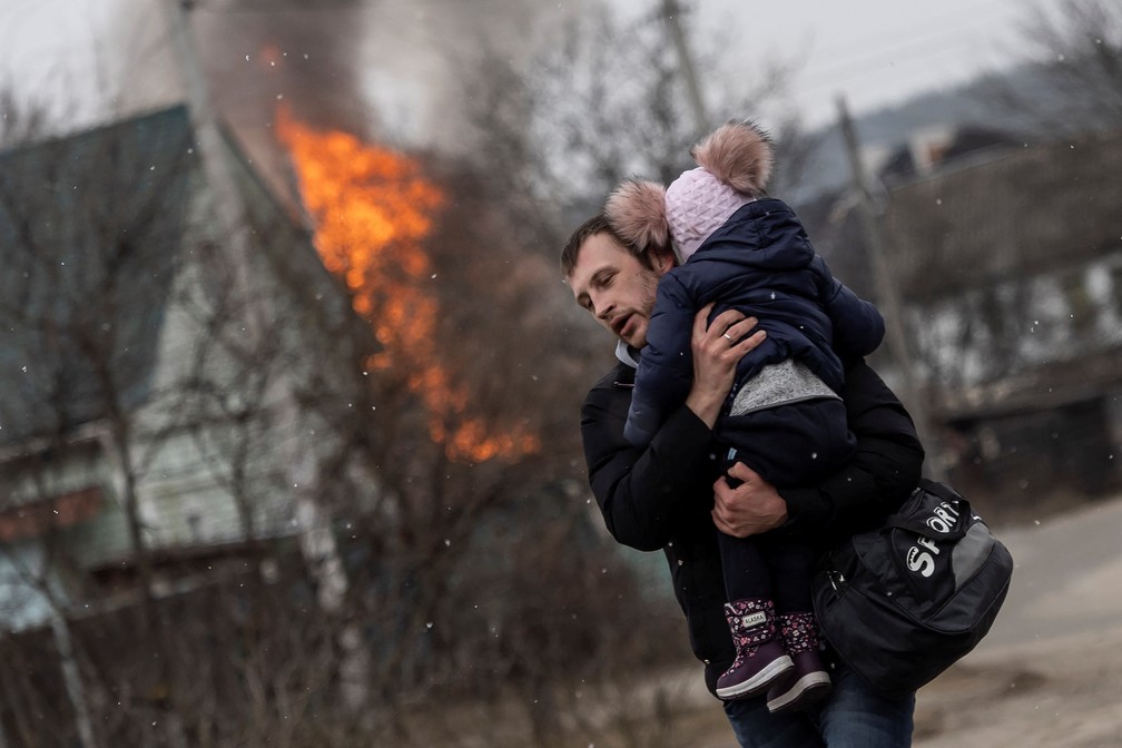 Um homem e uma criança fogem da cidade de Irpin, após bombardeios pesados na única rota de fuga usada por moradores, enquanto tropas russas avançam em direção à capital de Kiev, em Irpin, neste domingo (6) — Foto: Reuters/Carlos Barria