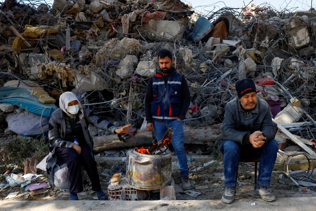 Diante de escombros, pessoas se aquecem em fogueira improvisada na cidade de Kahramanmaras, na Turquia — Foto: Suhaib Salem/REUTERS