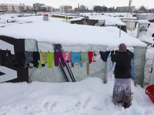 Uma mulher síria pendura roupas no varal do lado de fora de sua barraca coberta por neve em um campo de refugiados em Zahlé, no leste do Líbano. A neve na região já matou pelo menos dois refugiados (Foto: Hussein Malla/AP)