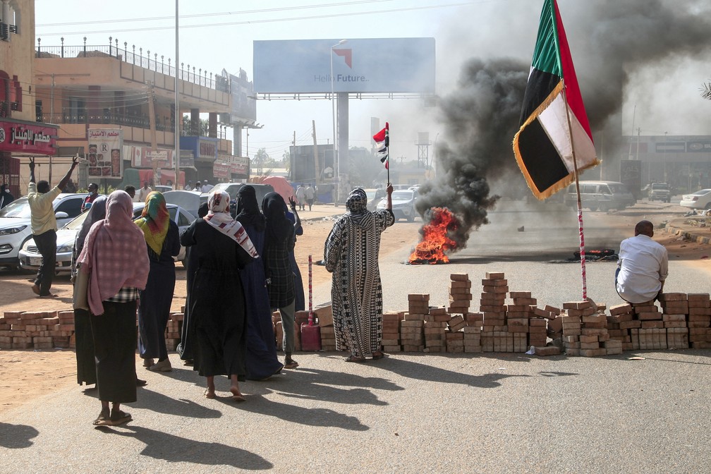 População ergue bandeiras do Sudão ao lado de um bloqueio com tijolos durante uma manifestação na capital Cartum, em 25 de outubro de 2021, contra o golpe militar — Foto: AFP
