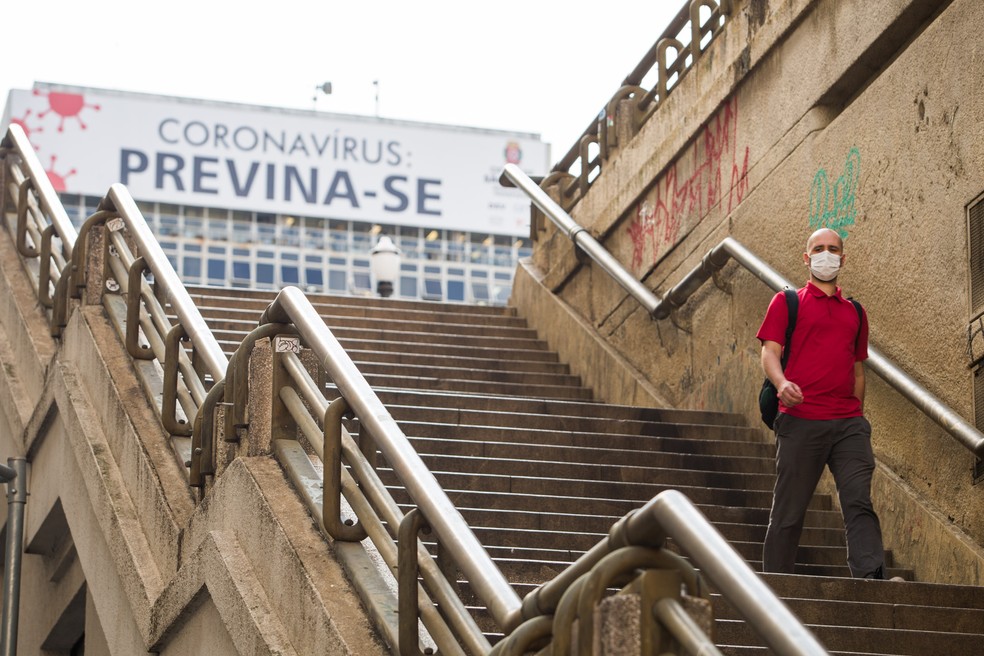 Paulistano desce escadaria de máscara, diante de cartaz sobre combate à epidemia causada pelo novo coronavírus — Foto: Tiago Queiroz/Estadão Conteúdo