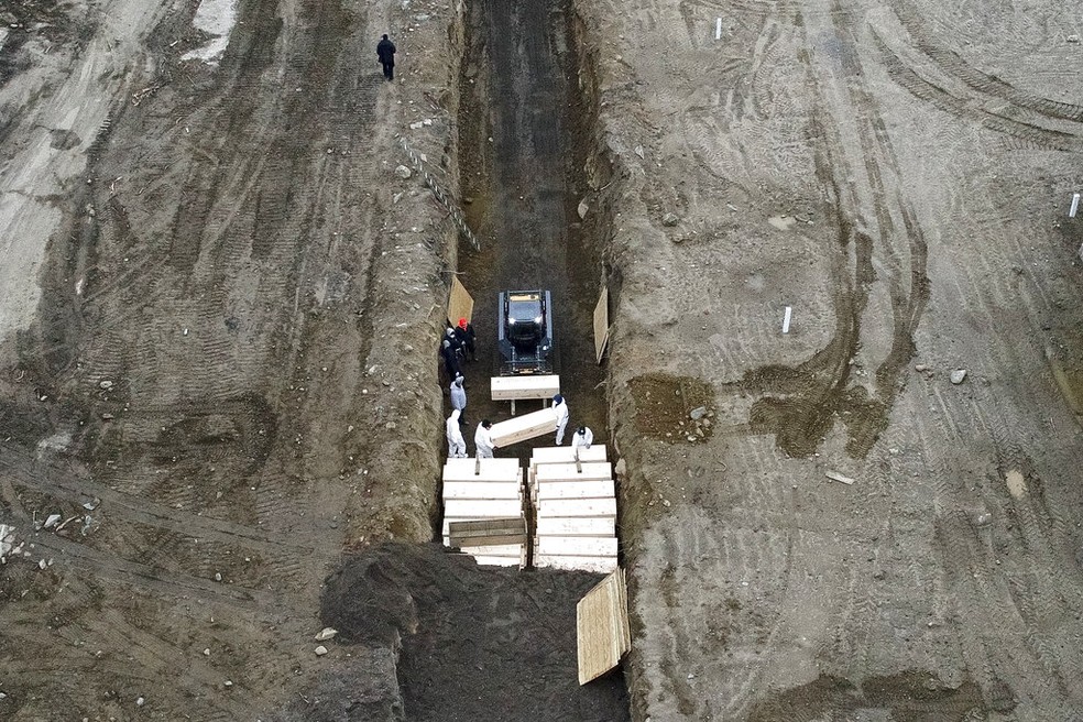  Trabalhadores enterram corpos em uma vala em Hart Island, no bairro do Bronx, em Nova York.  — Foto: AP Photo/John Minchillo