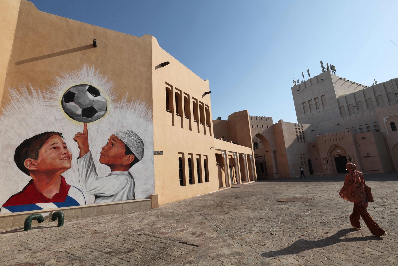 Mulher passa por um mural temático na Katara Cultural Village, em Doha, capital do Catar, que sediará a Copa do Mundo da Fifa — Foto: GIUSEPPE CACACE/AFP