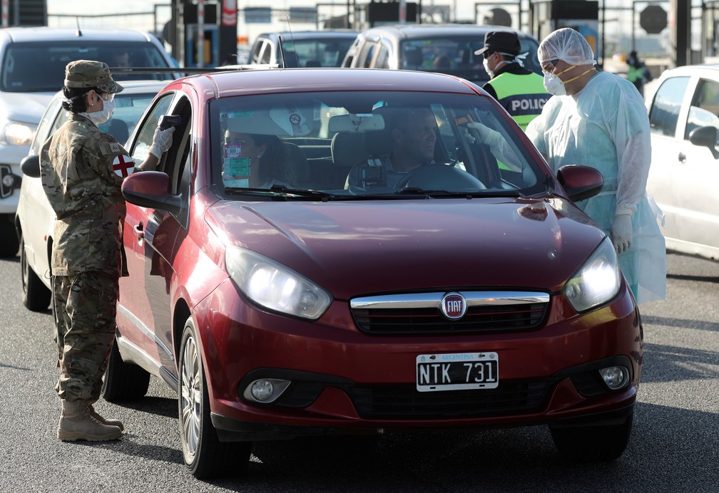 Policial e profissional de saúde checam motorista de carro que chega à Argentina nesta quinta-feira (19) em meio à pandemia do novo coronavírus — Foto: Agustin Marcarian/Reuters
