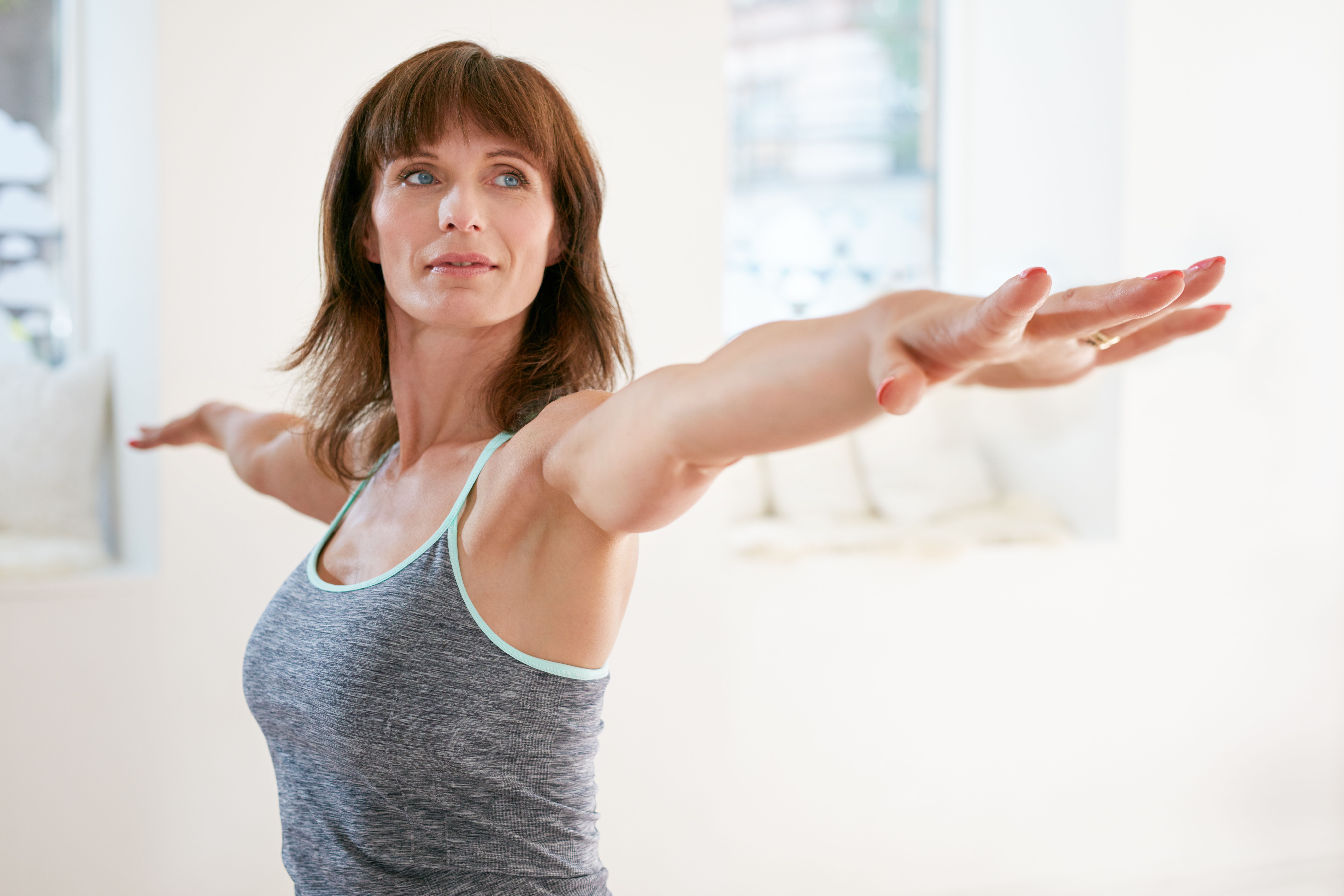 Portrait of mature woman stretching her arms and looking away at gym. Beautiful woman performing yoga in warrior pose, Virabhadrasana. (Foto: Getty Images/iStockphoto)